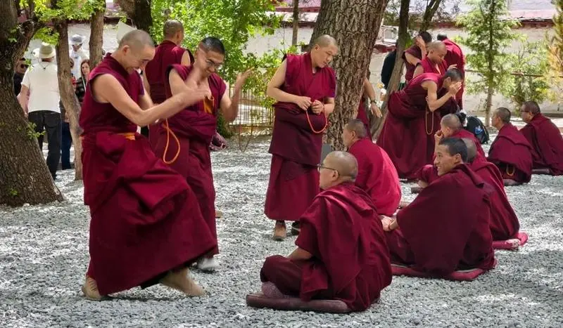 Monks debating in the courtyard of Sera Monastery in Lhasa, Tibet — maroon robes, hand-claps and an attentive circle