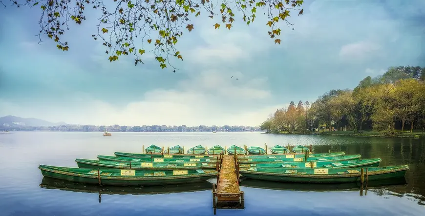 Green rowing boats moored at a wooden jetty on West Lake in Hangzhou