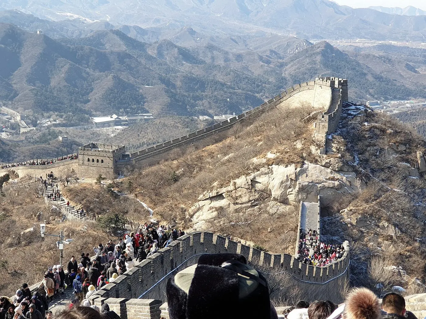 Travellers walking along the Great Wall of China on a clear winter morning, with watchtowers and mountain ridges behind them