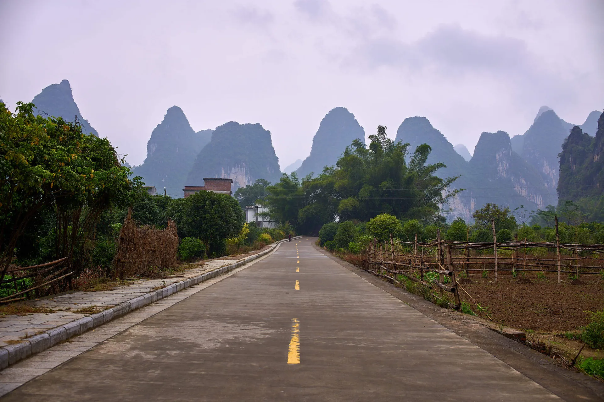 A country road in Guangxi running straight toward the karst limestone peaks of Yangshuo, fields and village houses on either side