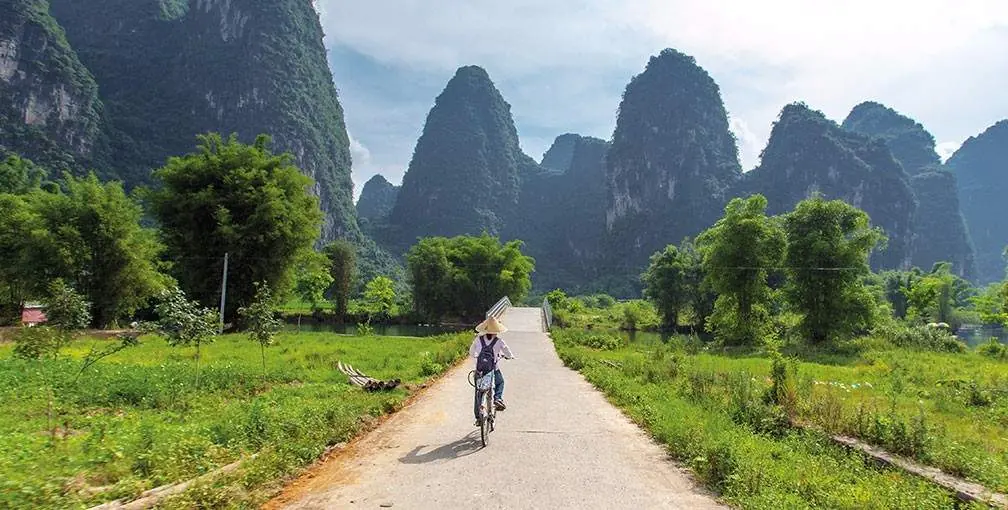 A cyclist on a country path in the Yangshuo countryside in Guangxi, green fields and karst limestone peaks all around