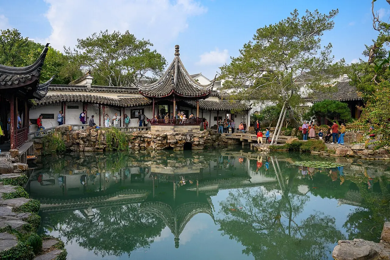 A pavilion reflected in the pond of the Master of the Nets Garden in Suzhou, with rockeries and white-walled halls